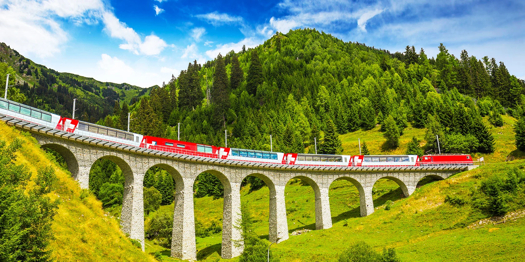 Glacier Express panorama cars crossing a curved stone viaduct through summer forest in the Swiss Alps